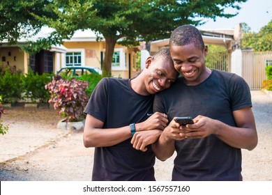 gay couple laughing together while using a phone together. two young black men walking and holding each other laughing together while viewing content on a mobile phone. - Powered by Shutterstock