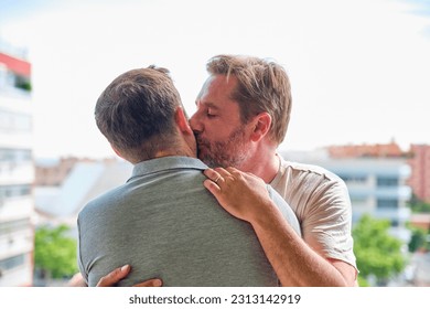 gay couple of mature boys on the terrace of their apartment hugging and kissing with the city in the background - Powered by Shutterstock