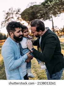 Gay Couple Of Men Having Fun Tickling Their Daughter Who Laughs.