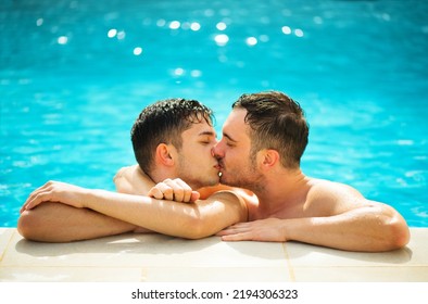 Gay Couple Relaxing In Swimming Pool. LGBT. Two Young Men Enjoying Nature Outdoors, Kissing And Hugging. Young Men Romantic Family In Love. Happiness Concept.