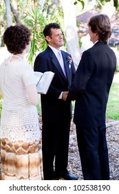 Gay Couple Saying Their Wedding Vows In Front Of A Young Female Minister.