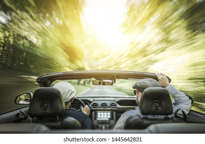 Gay Couple Summer Road Trip. Two Caucasian Men In A Modern Convertible Car Driving Through The Forest. Motion Blur Effect.