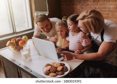 Gay Couple With Their Adopted Cute Daughters Reading Recipe On Laptop And Cooking On Kitchen. Lgbt Family At Home.