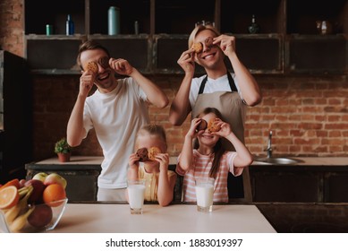 Gay Couple With Their Adopted Cute Daughters Cooking On Kitchen. Lgbt Family At Home. Portrait Of Two Handsome Men And Their Two Little Daughters Eating Cookies And Drinking Milk.