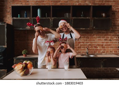 Gay Couple With Their Adopted Cute Daughters Cooking On Kitchen. Lgbt Family At Home. Portrait Of Two Handsome Men And Their Two Little Daughters Eating Cookies And Drinking Milk Wearing Santa Hat