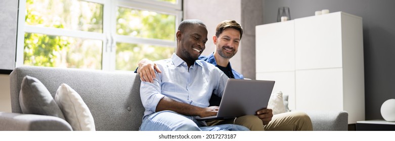 Gay Couple Using Computer For Video Conference On Sofa Or Couch