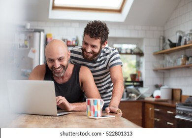 Gay couple using laptop in the kitchen - Powered by Shutterstock