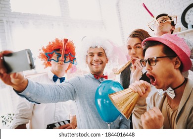 Gay guys in bow ties taking selfie on phone at party. Man in a wig stands in a room with friends and takes a photo in memory of a gay party. 