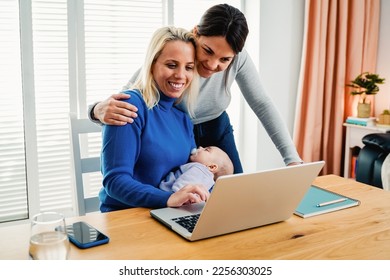 Gay lesbian couple of mothers and newborn baby working with laptop computer at home - Lgbt family concept - Focus on infant face - Powered by Shutterstock