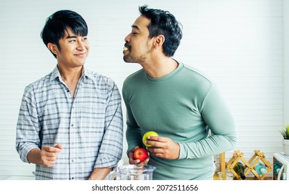 Gay LGBT Sweet Asian Couple Wearing Pajamas, Smiling, Teasing And Feeding Fruit By Mouth With Happiness And Love, Eating Healthy Fruits For Breakfast In Kitchen In The Morning. Lifestyle Concept