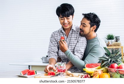 Gay LGBT Sweet Asian Couple Wearing Pajamas, Smiling With Happiness And Love, Eating, Feeding Watermalon, Healthy Fruit For Breakfast In Kitchen At Home In The Morning With Sunlight. Lifestyle Concept