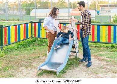 Gay Male Couple Playing With Their Children On The Slider