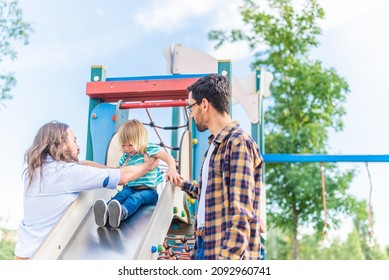 A Gay Male Couple With Their Son On The Slide