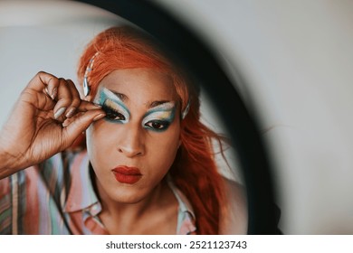 Gay man applying makeup tutorial video, beauty blogger, Gay man getting a drag queen makeup done for a livestream online. Passionate gay man putting on eye lashes in front of the mirror. - Powered by Shutterstock