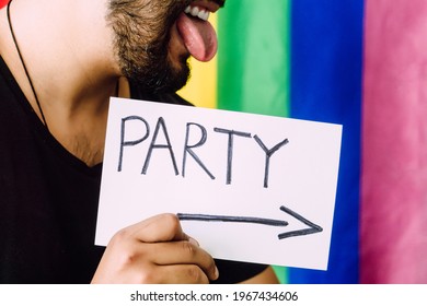 Gay Man Celebrating With A Paper In His Hand That Says Party, Lgbt Concept, Rainbow Colors Flag Background, Sticking Out His Tongue