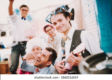 Gay Man Smiling While Playing Small Guitar For Friends. People Sit At Home And Have Fun At A Gay Party Together. 