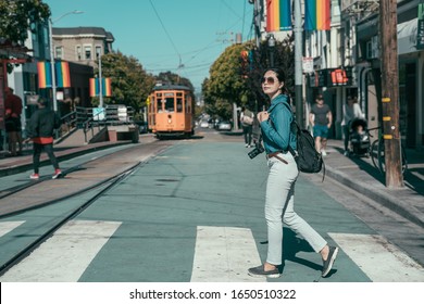 gay pride in castro district of San Francisco. young asian girl lesbian searching love while crossing pedestrian road in city. side view full length backpacker visit rainbow town against cable car