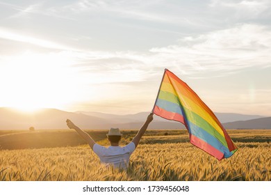 Gay Pride Concept. Man With 2 Arms Outstretched Moves The LGBT Rainbow Flag. Happiness And Freedom