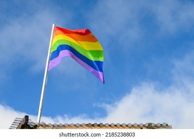 Gay Pride, Rainbow Flag Flying High Against A Sunny Blue Sky With Light White Clouds, Freedom Symbol 
