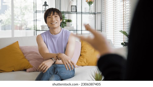 Gay queer asian man non-binary influencer sitting easy at home sofa. Asia non binary LGBT young guy adult two people happy relax smile talking asking advice face to face in mental health care therapy. - Shutterstock ID 2306387405