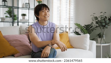 Gay queer asian man non-binary influencer sitting easy at home sofa. Asia non binary LGBT young guy adult two people happy relax smile talking asking advice face to face in mental health care therapy.