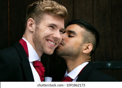 Gay Wedding, Grooms Posing For As They Hold Hands And Kiss Outside Village Church