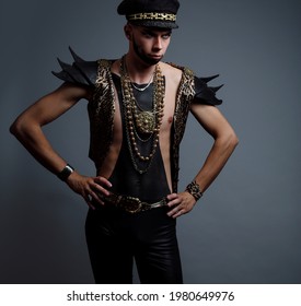 A Gay Young Man In A Vest And Leather Leggings On A Gray Background. Studio Photo.