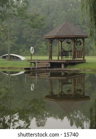 A gazebo and canoe reflected in a pond.