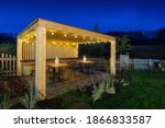 Gazebo with lights at night. Picture of a summer house with comfortable garden furniture. Romantic scene in dusk.