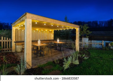 Gazebo With Lights At Night. Picture Of A Summer House With Comfortable Garden Furniture. Romantic Scene In Dusk.