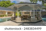 Gazebo in the recreation area by the swimming pool. A table and wicker chairs under a canopy. Around the perimeter there are villas with green vegetation on open terraces. Philippines.