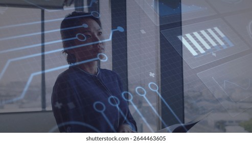 Gazing adult Asian businesswoman interacting with digital overlays in office, holding documents. Technology, innovation, corporate, futuristic, data, digital, professional