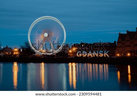 Gdansk Poland Ferris wheel in the old town of Gdansk at night evening dusk Reflection in river water Europe. Long exposure photo. City scenic view Illuminated attraction park and street