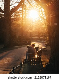 Gdansk,PL-15 Mar 22: Couple sitting on the Olive Park bench in golden hour sun, male and female having a discussion while sitting on a bench, man looking at his phone - Shutterstock ID 2152871197