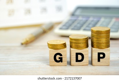 GDP Or Gross Domestic Product In Wooden Block Letters On Coins On Desk Background With Calculator Notebook Pen On Business Background.                                                 