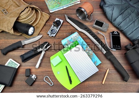 Gear laid Out For Backpacking Trip On  Table. Items Include Rope Bag Backpack  Raincoat Vest Notepad Compass Wallet Money Binoculars Knife Machete Searchlight Flashlight Rope Pen Pencil Mug Map