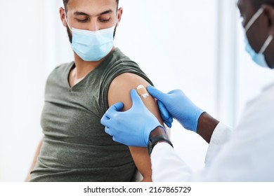 Gearing Up For A Global Scale Vaccination. Shot Of A Doctor Applying A Band Aid After Injecting A Patient In His Arm During A Consultation At A Clinic.