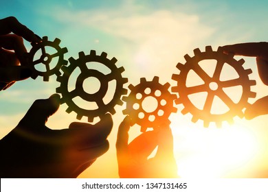 Gears In The Hands Of People Against The Sky. Teamwork, Interaction.