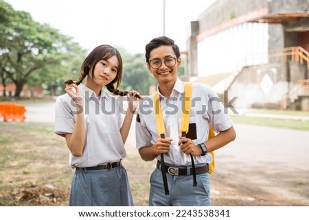 Geeky boy student in glasses smiling with girl friends in uniform on outdoor background