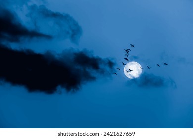 Geese flying in front of a full moon at night with dark clouds and night blue sky background - Powered by Shutterstock