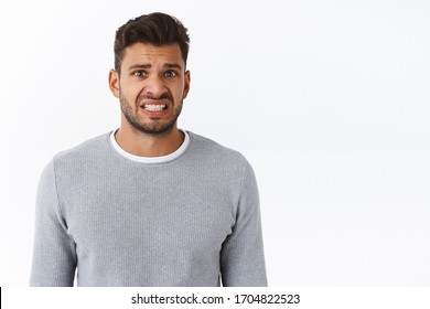 Geez thats bummer. Upset awkward handsome gay man in grey sweater, clench teeth with nervous smile, grimacing sad and disappointed, frowning express his condolences or apologizing for making mistake - Shutterstock ID 1704822523