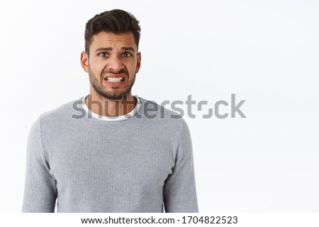 Geez thats bummer. Upset awkward handsome gay man in grey sweater, clench teeth with nervous smile, grimacing sad and disappointed, frowning express his condolences or apologizing for making mistake