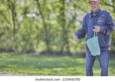 GEILENKIRCHEN, GERMANY - Apr 16, 2022: A Beautiful Shot Of An Old Caucasian Man Feeding The Ducks In The Park On A Beautiful Sunny Day In Geilenkirchen, Germany