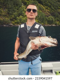 GEIRANGER, NORWAY - Aug 24, 2019: The Fisherman On A Boat Holding On Hand A Fish In The Sea In Norway In Summer