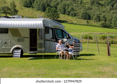 Geiranger, Norway - June 26 2018: A Campervan Or Motorhome In A Geiranger Camping RV Park In Summertime. Older Couple Having A Lunch In Norwegian Fjords.