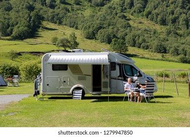 Geiranger, Norway - June 26 2018: A Campervan Or Motorhome In A Geiranger Camping RV Park In Summertime. Older Couple Having A Lunch In Norwegian Fjords.