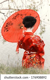 Geisha With Red Umbrella At The River Bank (back View)