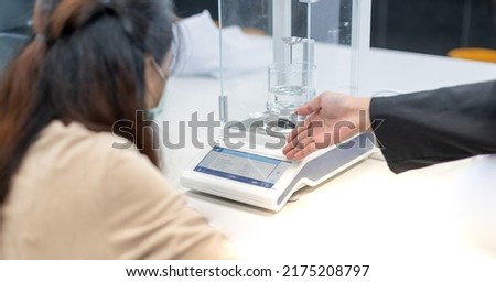 The gemologist shows the method of using the Hydrostatic Weighing Balance to study the specific gravity of the precious stone.