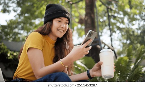 Gen Z eco go green woman asia sit happy relax at tree public park city life enjoy typing mobile phone drink coffee bottle use reuse tote bag care save the earth planet net zero waste clean future hope - Powered by Shutterstock