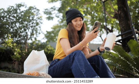 Gen Z eco go green woman asia sit happy relax at tree public park city life enjoy typing mobile phone drink coffee bottle use reuse tote bag care save the earth planet net zero waste clean future hope - Powered by Shutterstock